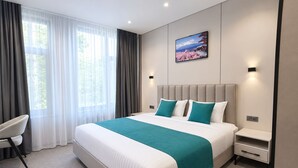 Habitación de hotel con una cama grande, un escritorio y una silla. Hay un cuadro en la pared y una ventana con cortinas.