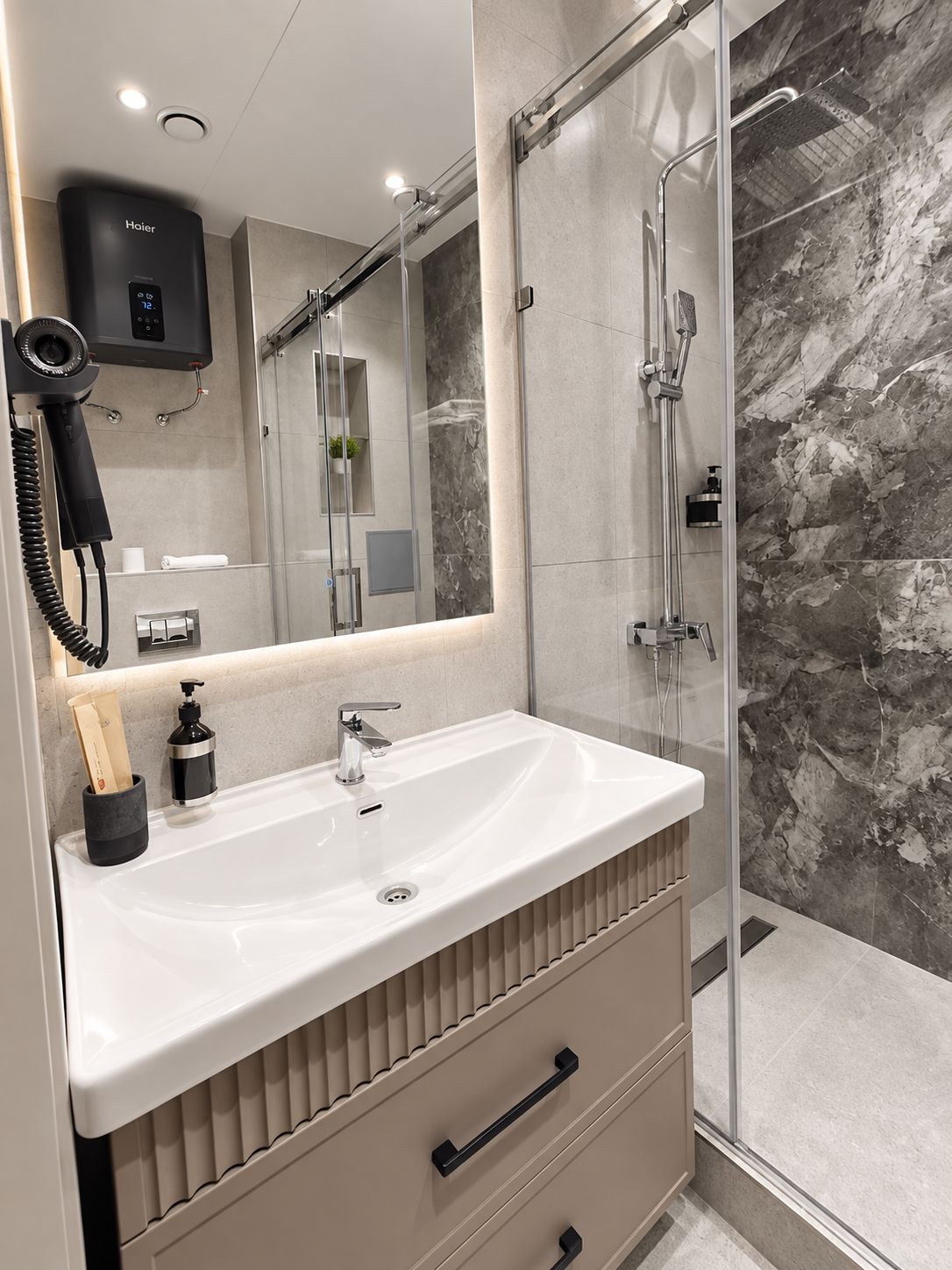 Un baño moderno con lavamanos blanco, espejo, secador de pelo y zona de ducha.