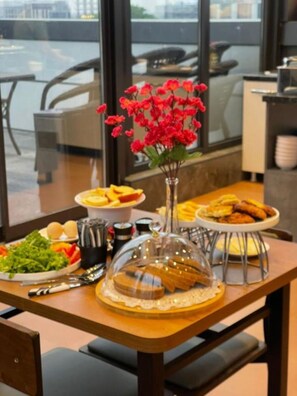 A dining table with various dishes, a vase with red flowers, and a glass dome covering a pastry display. - Tokyo Hotel (Bishkek)