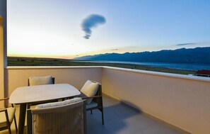 Ein Balkon mit Tisch und Stühlen mit Blick auf eine Küstenlandschaft, in der Ferne Berge.