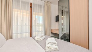Ein Hotelzimmer mit Bett, Nachttisch, Spiegel und leichtem Vorhang.