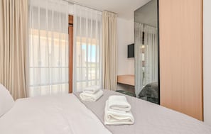 Ein Hotelzimmer mit Bett, Nachttisch, Spiegel und leichtem Vorhang.