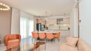 Ein modernes Wohnzimmer mit Essbereich, Küche und großen Fenstern mit Vorhängen.