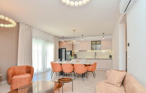 Ein modernes Wohnzimmer mit Essbereich, Küche und großen Fenstern mit Vorhängen.