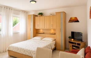 Ein Schlafzimmer mit einem Bett, einem Fernseher, einem TV-Schrank, einem Kleiderschrank und einem Fenster mit Vorhängen.