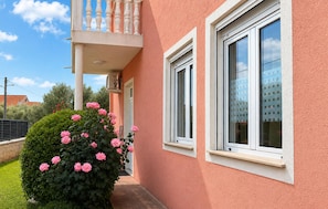 Ein Gebäude mit Balkon, Fenstern und einem Garten mit rosa Blumen.