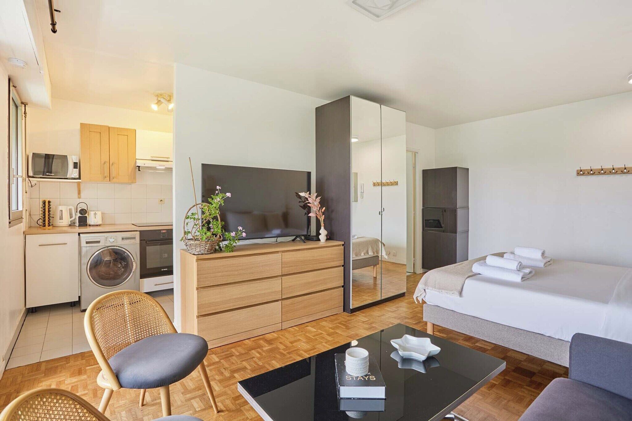 Ein kompaktes Hotelzimmer mit Bett, kleinem Schreibtisch, Fernseher, Kleiderschrank und einer Küchenzeile.