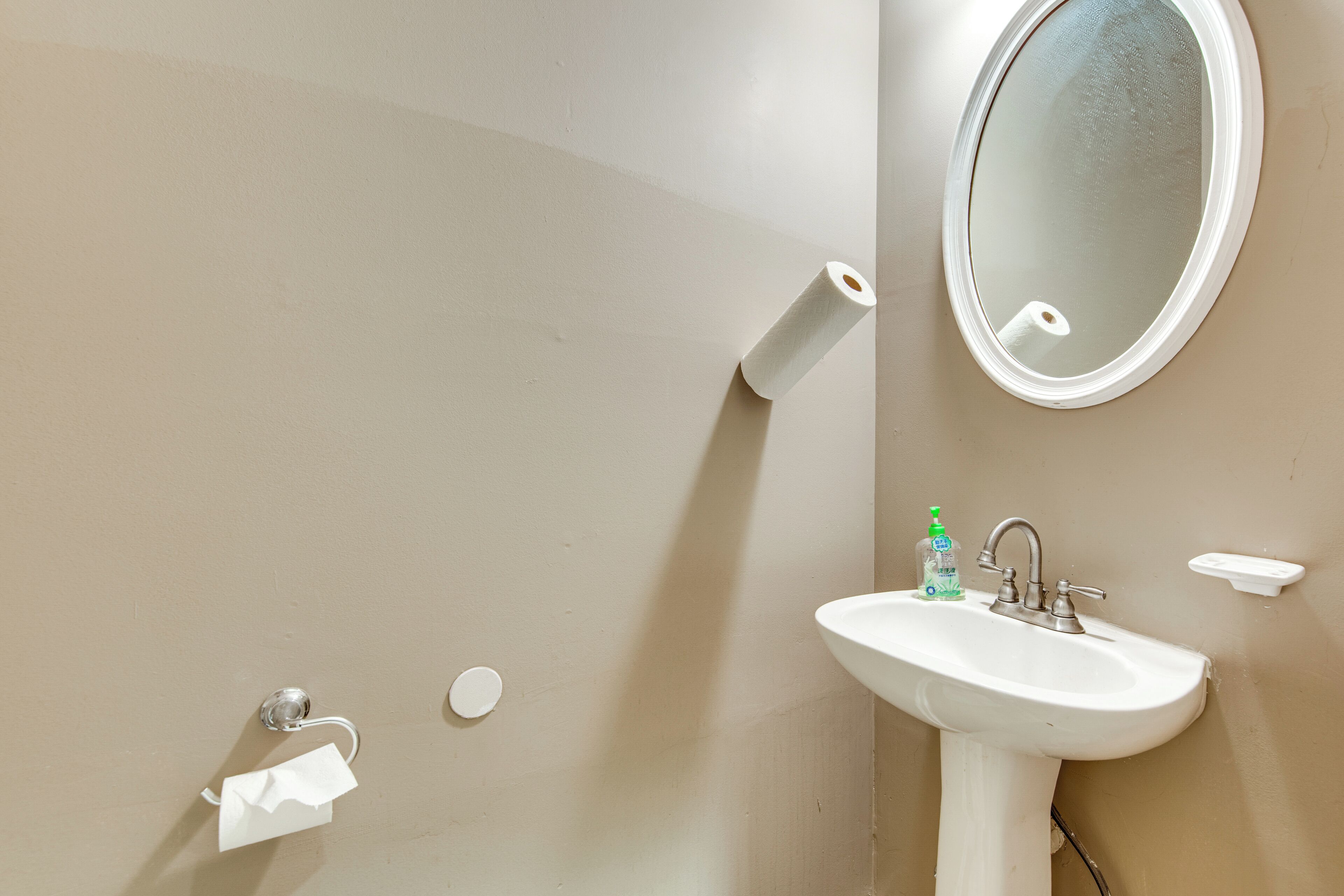 Un baño con lavamanos, espejo, papel higiénico y dispensador de jabón.