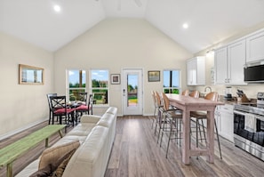 A spacious kitchen with a dining area, a bench, and a view through the door. - Bay Views + Sunset Deck | Pool Access | Padre Island, TX | Laguna Sunset (Corpus Christi)