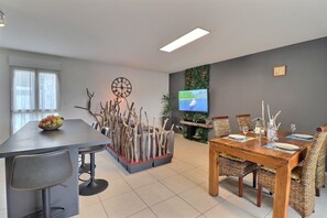 A modern dining area with a wooden table, wicker chairs, a television, and a decorative plant arrangement. - Evasion Tropicale (Ajaccio)