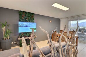 Ein modernes Wohnzimmer mit Flachbildfernseher, grauem Sofa, Holzeinrichtung und einem Essbereich mit Korbmöbeln.