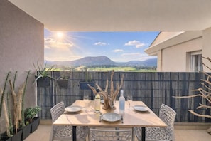 An outdoor dining area with a table set for four, surrounded by chairs, with a view of a mountainous landscape. - Evasion Tropicale (Sarrola-Carcopino)