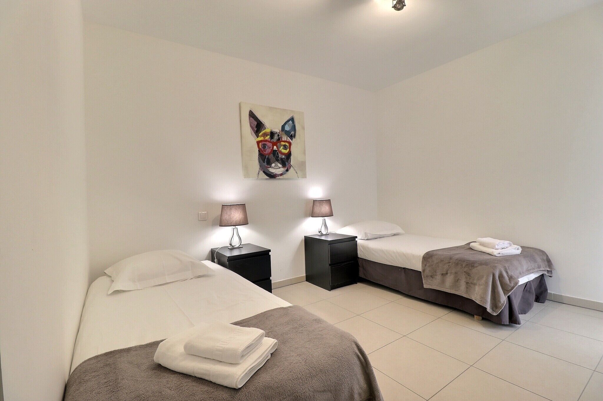 Una habitación de hotel con dos camas, un cuadro en la pared y lámparas de noche.