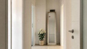Un couloir avec une plante en pot, un miroir et une porte dotée d’une poignée moderne.