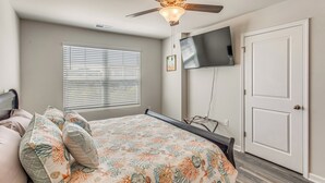 Une chambre à coucher avec un lit, un ventilateur de plafond, un téléviseur fixé au mur et une porte.