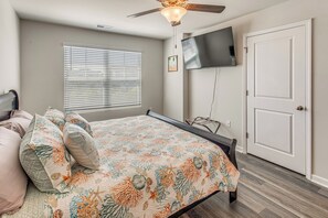 Ein Schlafzimmer mit einem Bett, einem Deckenventilator, einem Fernseher an der Wand und einer Tür.