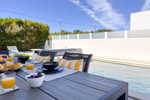 Ein Essbereich am Pool mit Tisch, gedeckt für das Frühstück, mit Croissants, Obst und Saft.