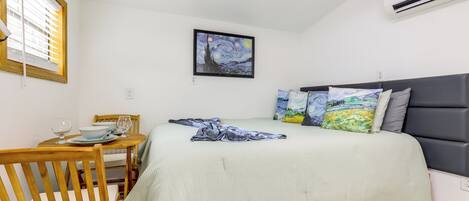 Un dormitorio con cama, un cuadro, una mesa de comedor con sillas y un equipo de aire acondicionado.