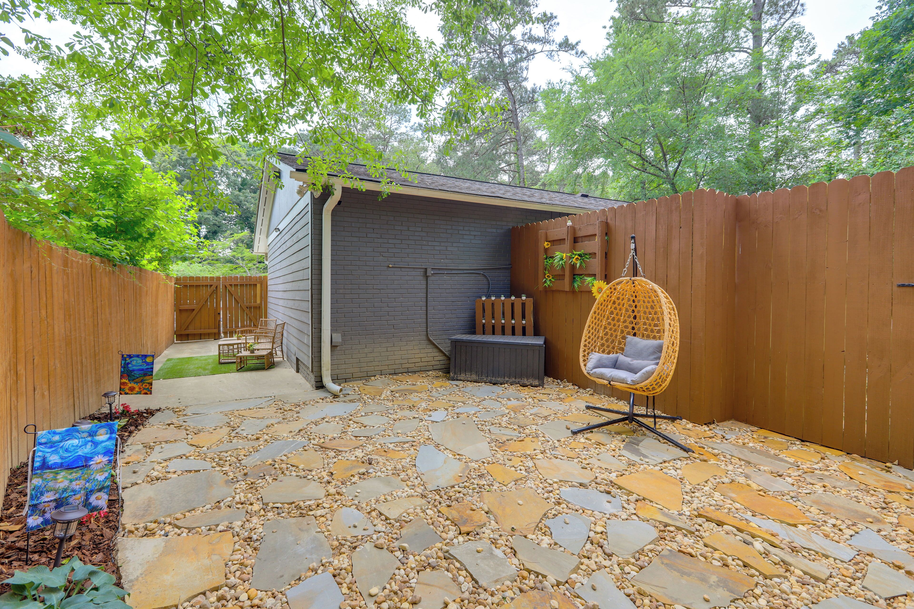 A backyard with a stone patio, a wooden fence, a hanging chair, and a small shed.