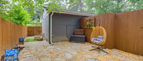 A backyard with a stone patio, a wooden fence, a hanging chair, and a small shed.