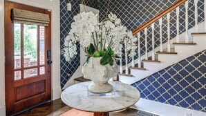 Taula de marbre amb un vas blanc de flors, una porta de fusta i una escala amb un mur estampat.
