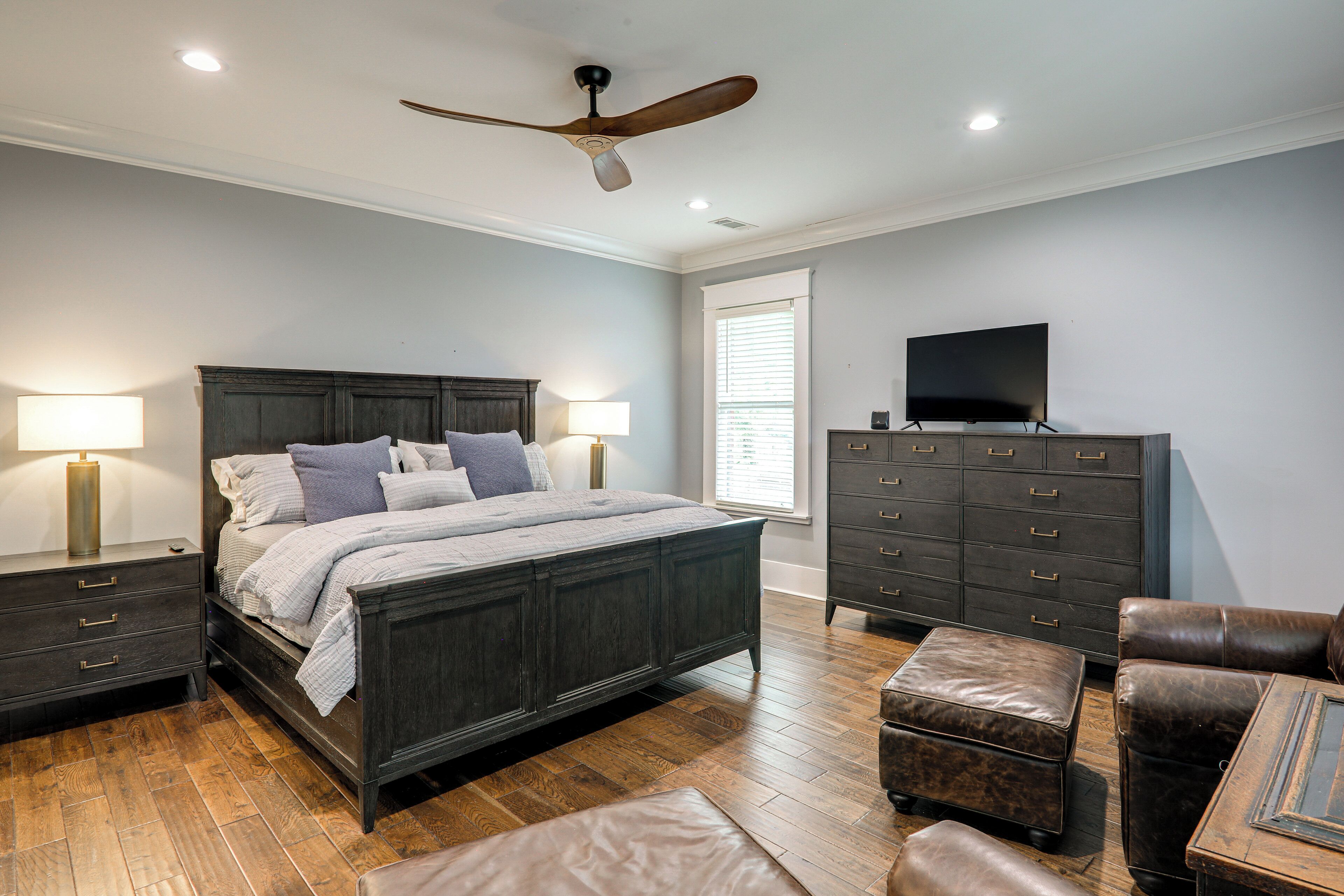 A bedroom with a bed, dresser, TV, and a ceiling fan.