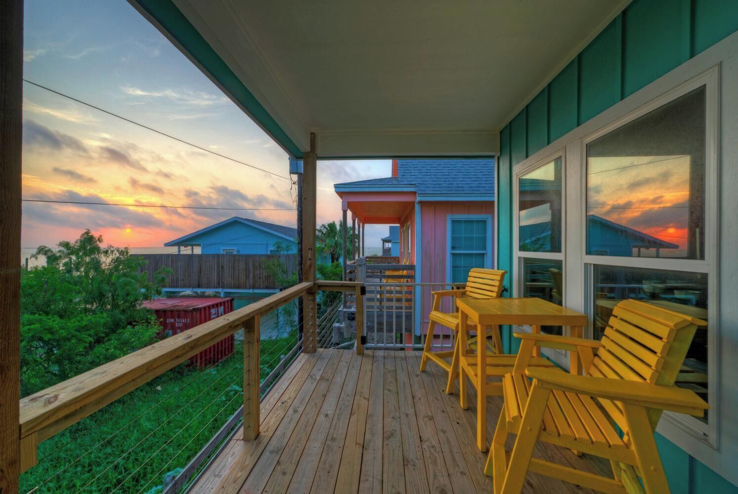 A wooden deck with outdoor furniture, a covered area, and a view of houses and sky.