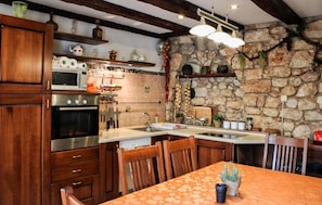 A kitchen with wooden cabinets, a stone wall, and a dining area with a table. - 2 bedroom gorgeous home in Grizane-Belgrad (Grizane-Belgrad)