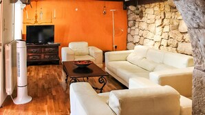 Ein Wohnzimmer mit einer Steinwand, weißen Ledersofas, einem Holztisch und einem Fernseher.