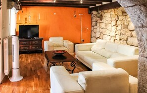 A living room with a stone wall, white leather sofas, a wooden coffee table, and a television. - 2 bedroom gorgeous home in Grizane-Belgrad (Grizane-Belgrad)