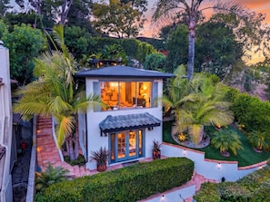 A modern house with a patio, surrounded by lush greenery and palm trees. - Designer Home + Backyard Oasis + Firepit | Mins to Universal | Laurel Terrace (Los Angeles)