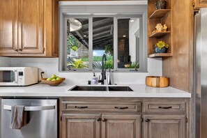 A kitchen with wooden cabinets, a built-in microwave, a sink, and a window overlooking a garden. - Designer Home + Backyard Oasis + Firepit | Mins to Universal | Laurel Terrace (Los Angeles)
