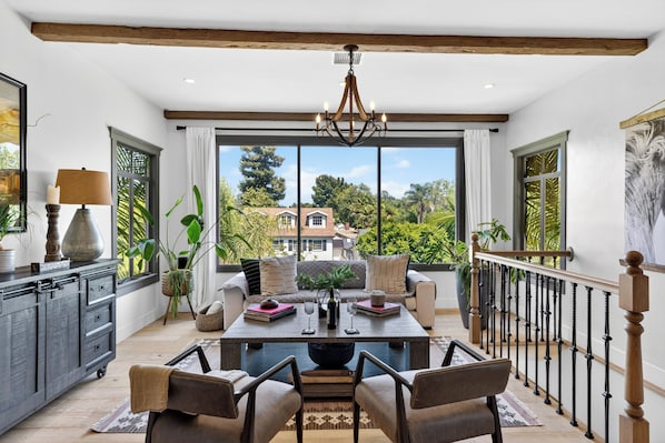 A spacious room with a large dining table, a chandelier, and a balcony with a view of the neighborhood. - Designer Home + Backyard Oasis + Firepit | Mins to Universal | Laurel Terrace (Los Angeles)