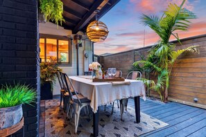 An outdoor patio with a table set for two, surrounded by potted plants and a wooden fence. - Designer Home + Backyard Oasis + Firepit | Mins to Universal | Laurel Terrace (Los Angeles)