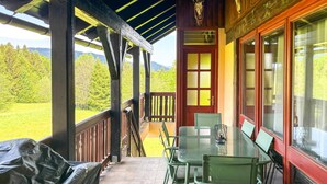 Eine überdachte Veranda mit Tisch und Stühlen, eine rote Tür und Blick auf eine grüne Landschaft.