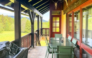 Eine überdachte Veranda mit Tisch und Stühlen, eine rote Tür und Blick auf eine grüne Landschaft.