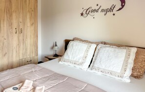 Ein Schlafzimmer mit Bett, Kissen, Nachttisch, Lampe, Kleiderschrank und Wandbild.
