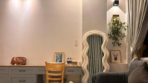 Una habitación con escritorio, sillón, sofá y una mesita con un jarrón.