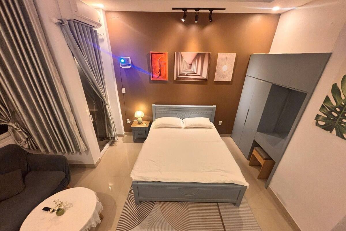 A hotel room with a bed, a TV, a nightstand with a lamp, a sofa, and artwork on the walls.