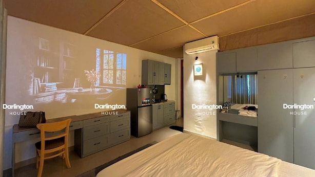 Un dormitorio con cama, escritorio, silla, armario y una pantalla de proyección mostrando una habitación.
