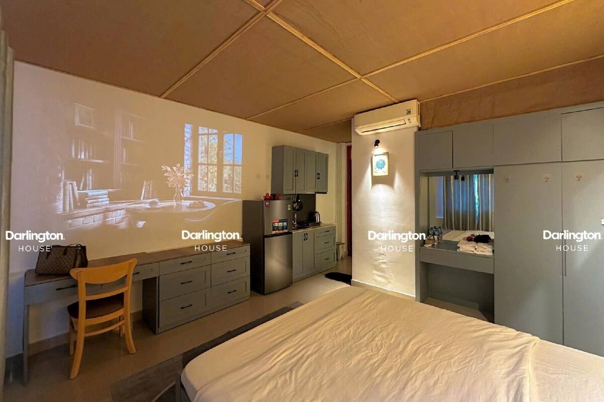 A bedroom with a bed, a desk, a chair, a wardrobe, and a projection screen displaying a room.
