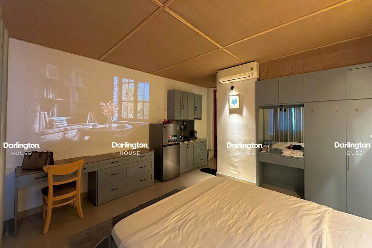 A bedroom with a bed, a desk, a chair, a wardrobe, and a projection screen displaying a room.