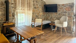 Habitació acollidora amb paret de pedra, una taula de fusta, un sofà, una cadira, un llit i un televisor fixat a la paret.