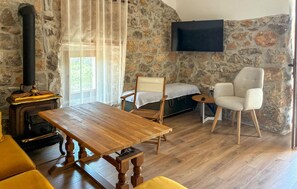 Ein gemütliches Zimmer mit Steinwand, Holztisch, Sofa, Sessel, Bett und Wandfernseher.