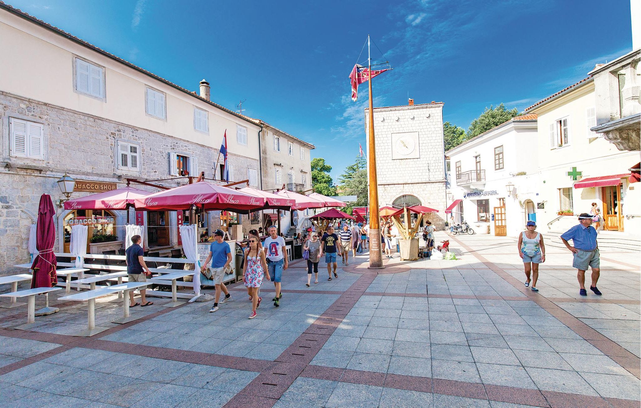 A public square with outdoor seating, shops, and a flagpole.