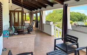 A balcony with a view of greenery, a chair, a table, and a hanging chair. - Stunning home in Dobrinj (Dobrinj)