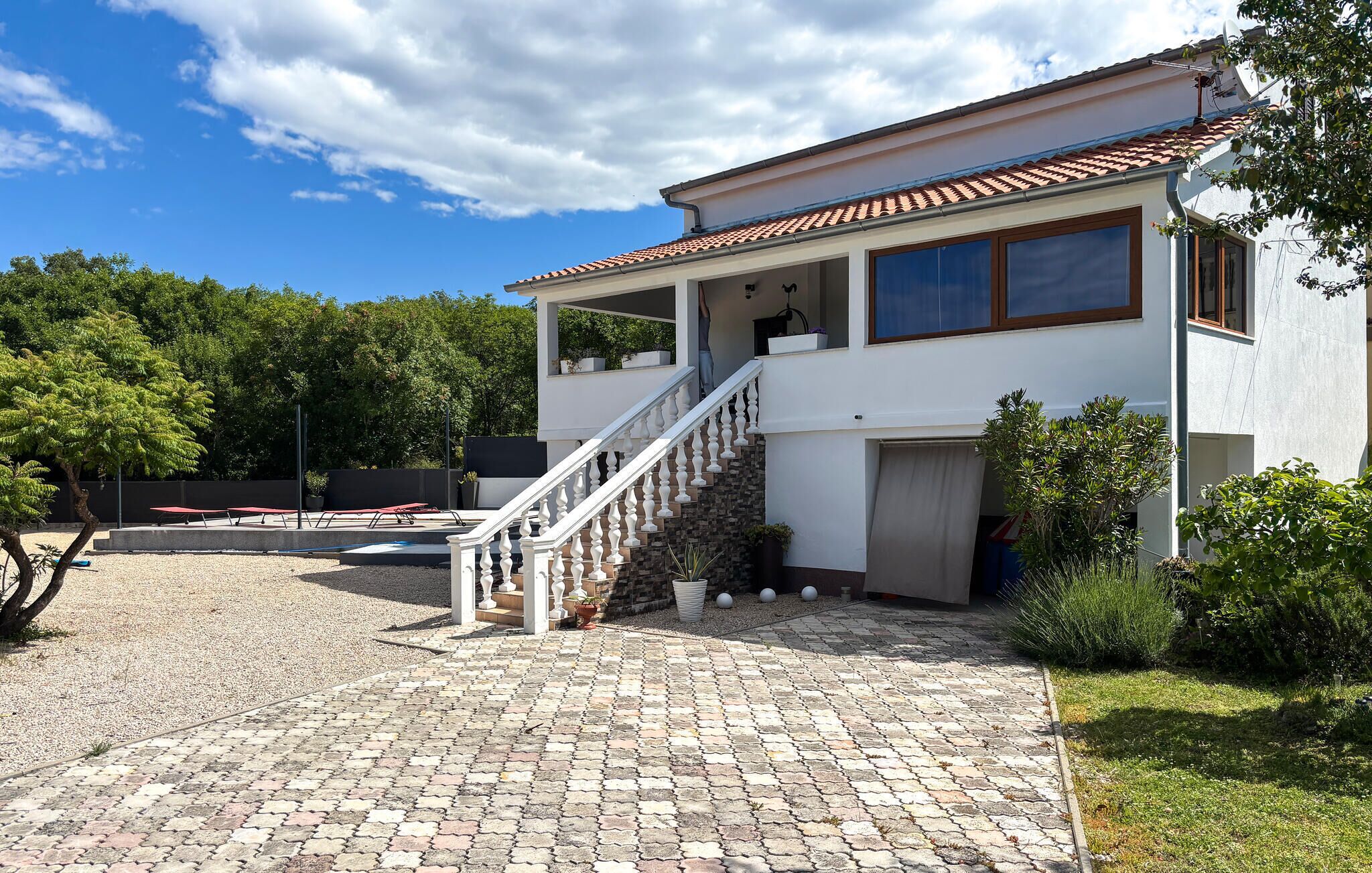 Une maison à deux étages, avec une façade blanche, un toit en tuiles et une cour pavée de pierres.