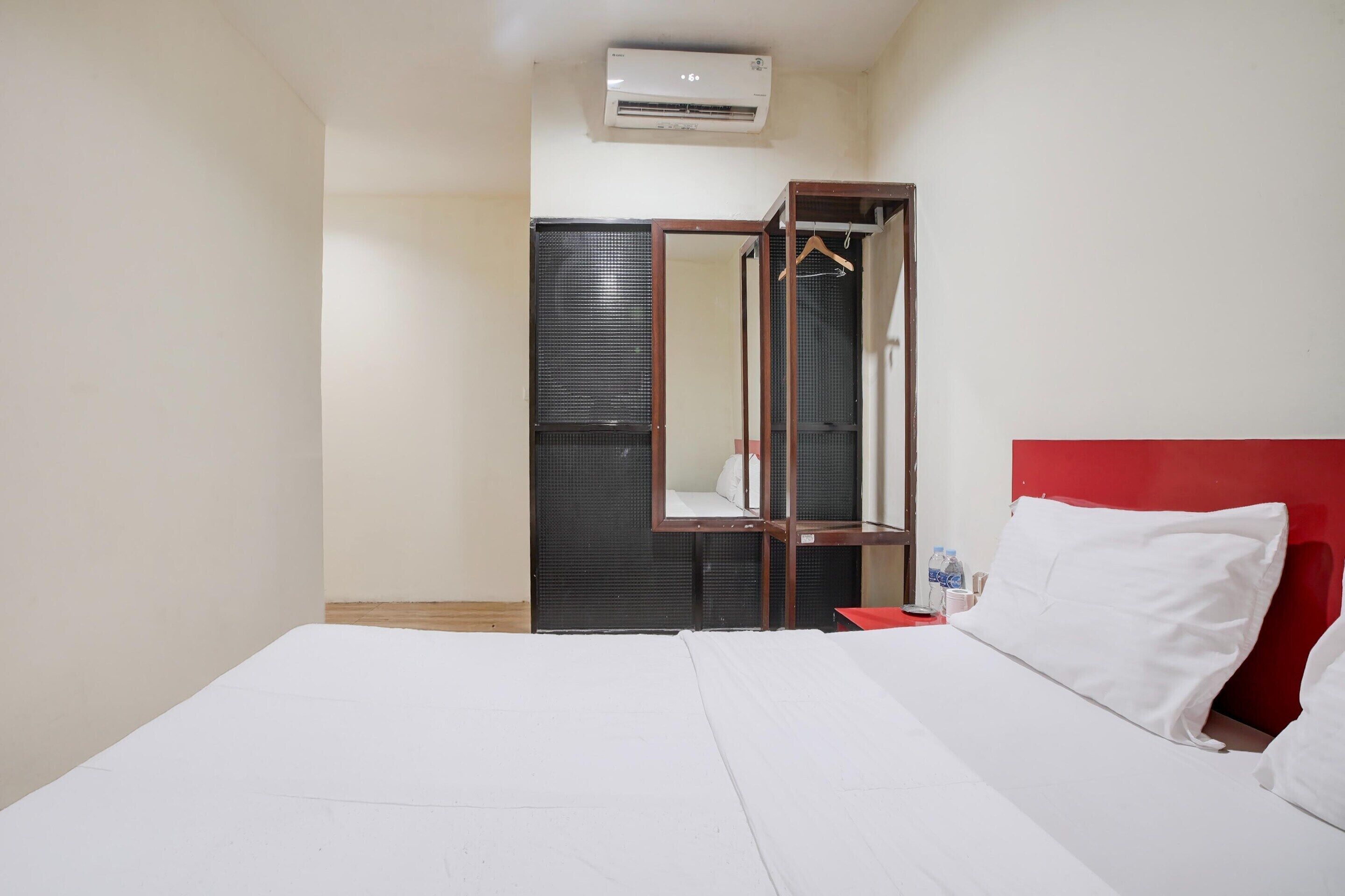 Hotellihuone, jossa on sänky, punainen pääty, vaatekaappi ja ilmastointilaite.