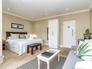A bedroom with a bed, bedside table, nightstand, wardrobe, and a small table with a lamp. - Hermanus Cliff Path Lodge (Hermanus)