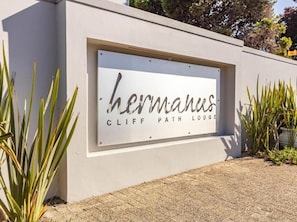 A sign for 'Hermanus Cliff Path Lodge' with a modern design and a clear view of the surrounding landscape.